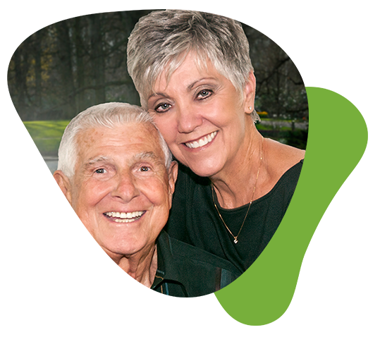 An older couple happily posing against a green backdrop, radiating joy and contentment.